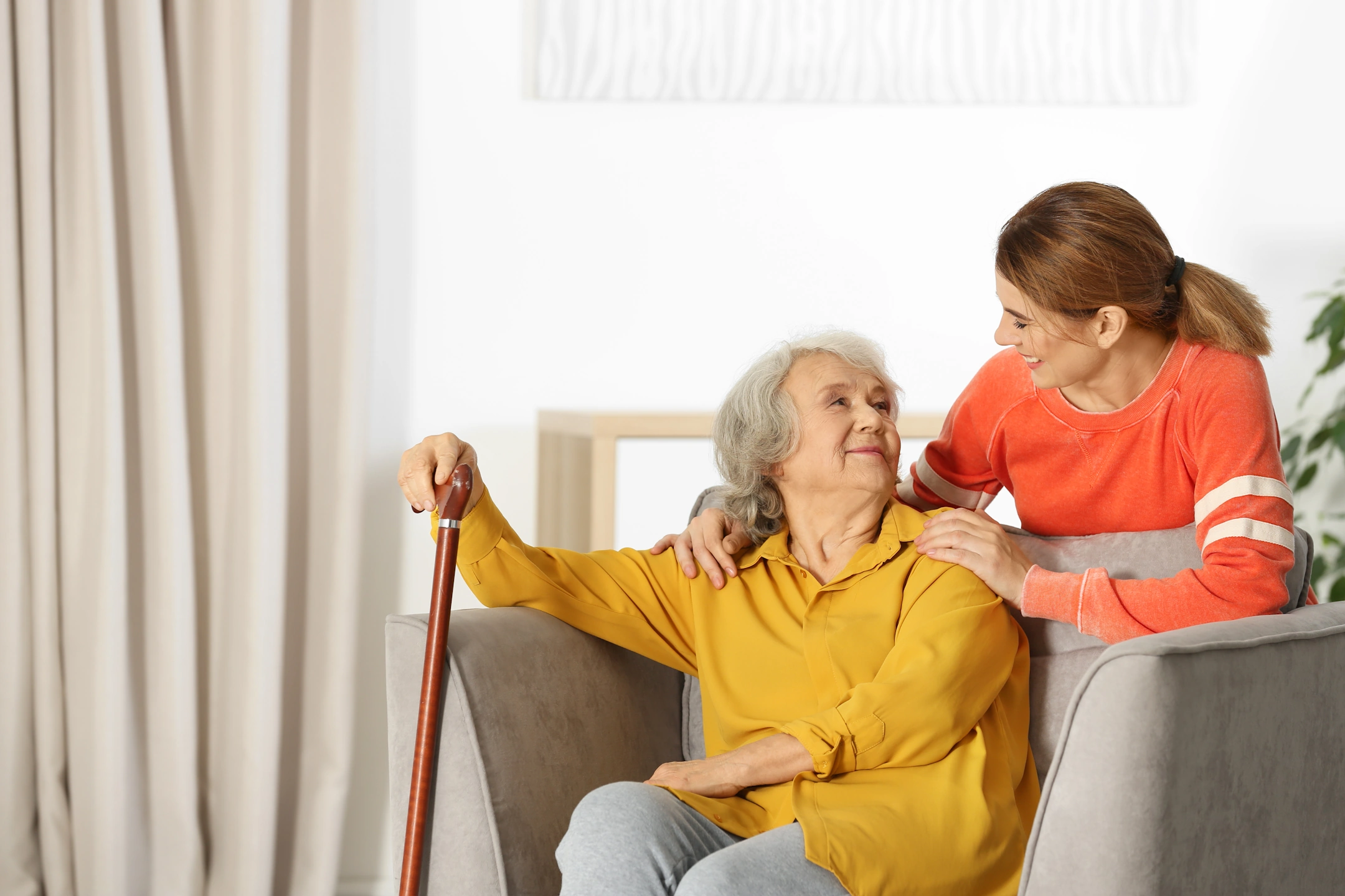 senior-home-care-agencies-Pipersville-PA-1-flipped Caregiver offering compassionate companionship to an elderly woman using a cane in a comfortable home.